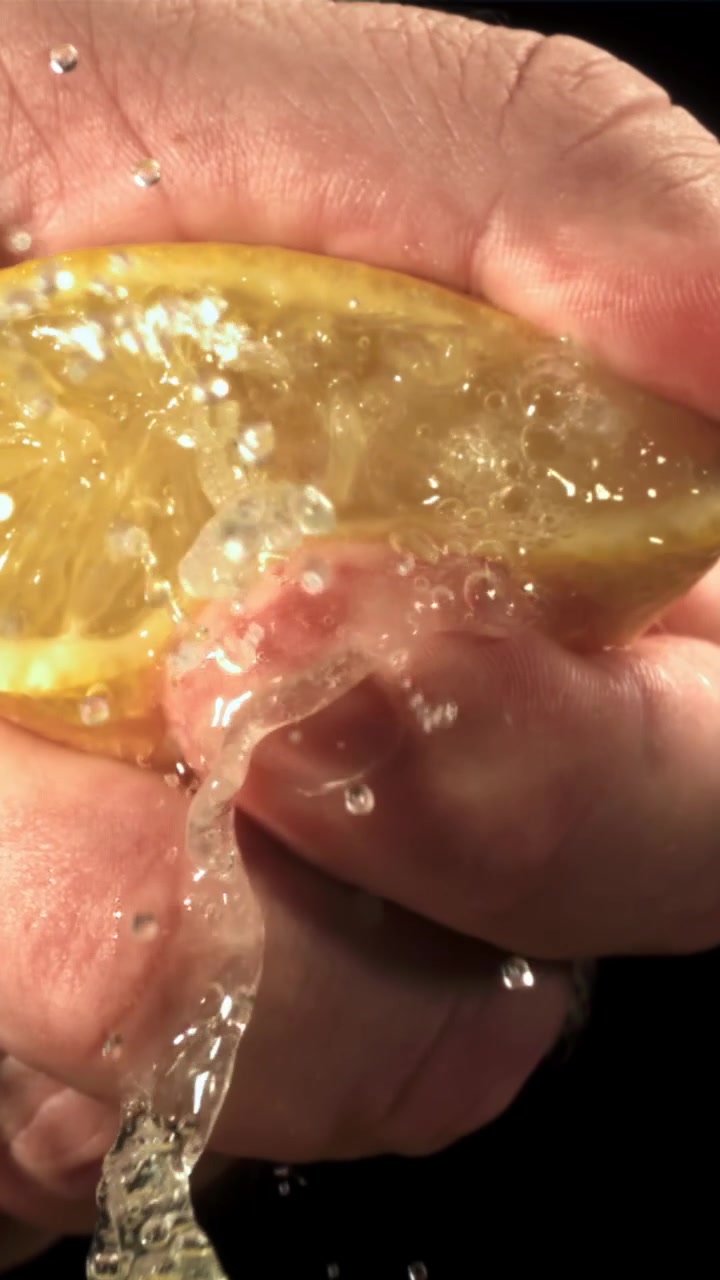 Primer plano en cámara lenta de una mano exprimiendo jugo de limón fresco