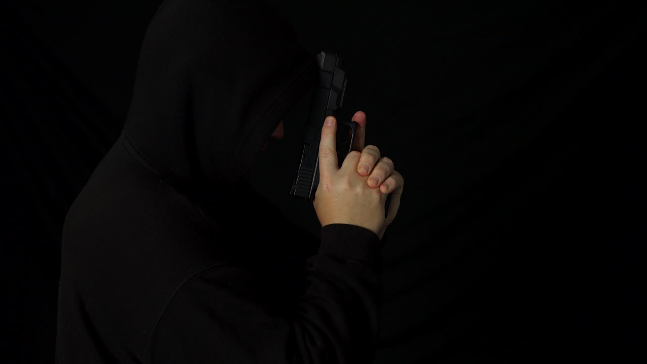 어둠 속에서 손으로 총을 든 두건을 쓴 남자