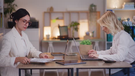 two women work late in corporate office on laptops