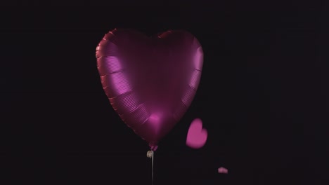 globo con forma de corazón de color rosa con corazones que caen aislado sobre fondo negro