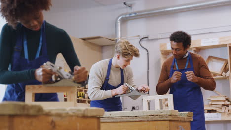 tutor with carpentry student in workshop studying for apprenticeship at college using wood plane