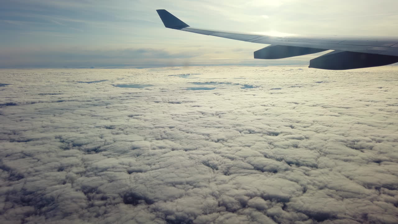 Experience the stunning view from an airplane wing as it soars above a blanket of clouds during a breathtaking sunset. The sky is painted with beautiful colors