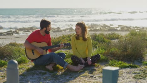 man playing guitar for woman near beach on a sunny day 4k