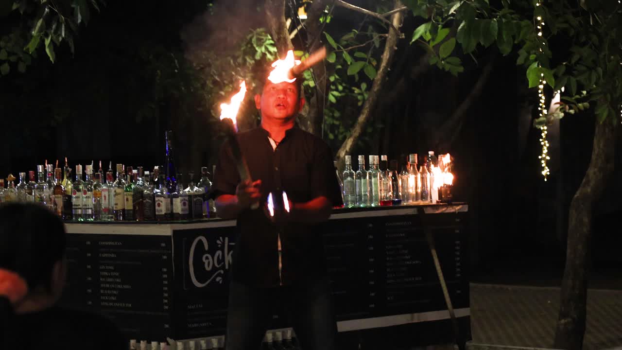 bartender haciendo malabarismos con botellas en llamas por la noche