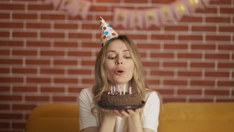 Portrait-of-pretty-girl-holding-birthday-cake-and-blowing-candles-at-party