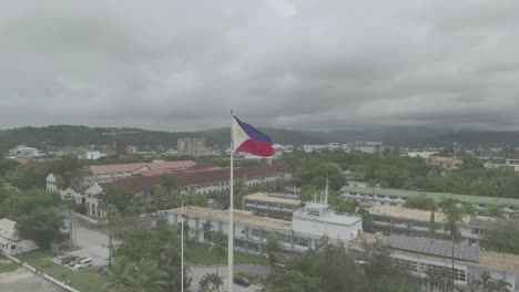 a breathtaking drone shot captures the philippine flag waving proudly atop a vibrant green landscape, with dramatic clouds framing the scene, highlighting the nation's rich culture and natural beauty.