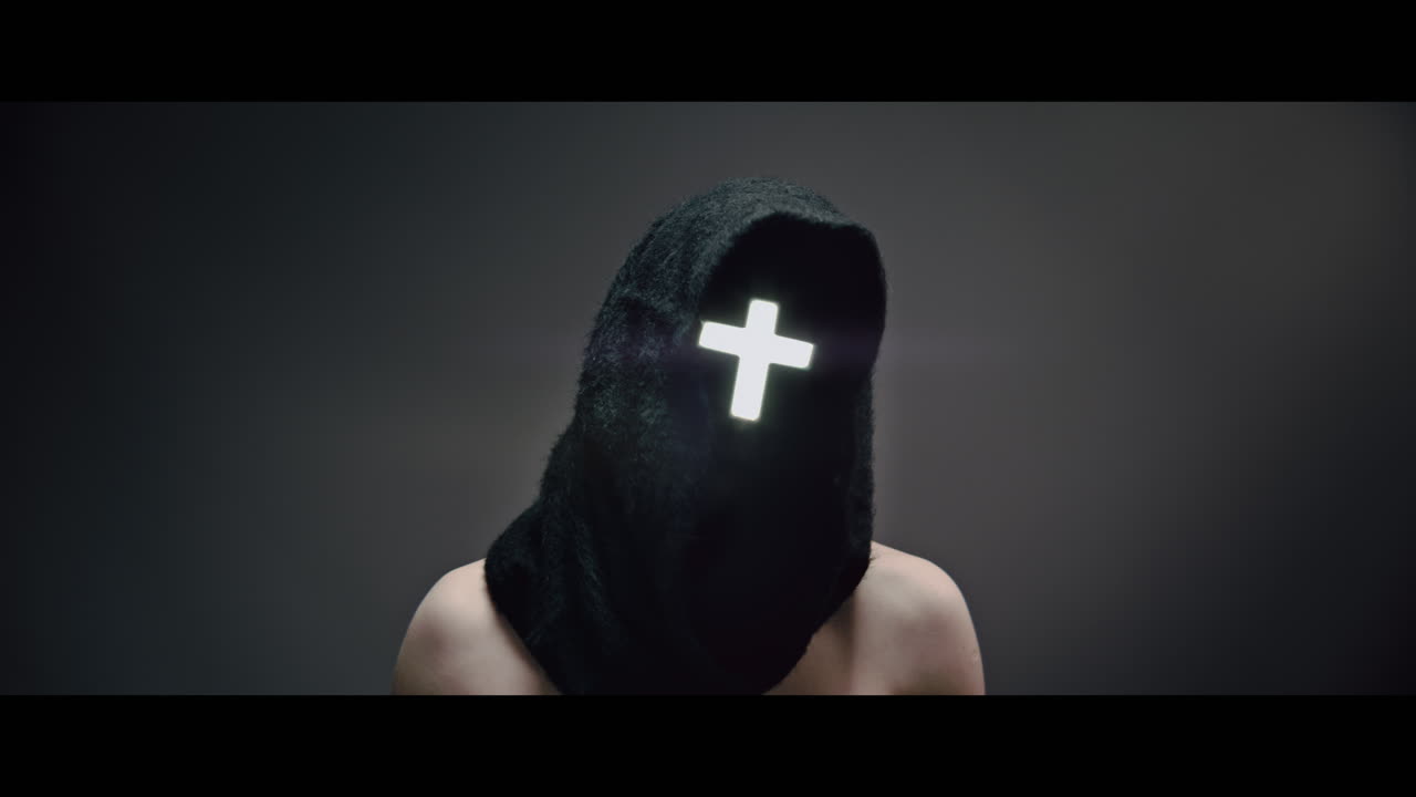 Masked and hooded man with cross of light glowing on his face rise his head