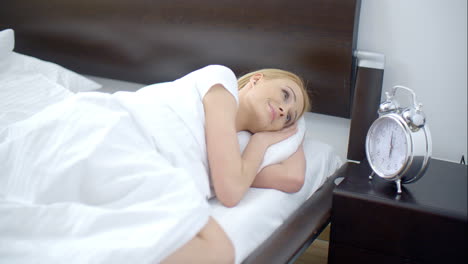 una mujer bonita durmiendo con un despertador a su lado.