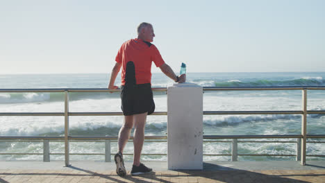 Hombre-Mayor-Sosteniendo-Una-Botella-De-Agua-De-Pie-En-El-Paseo-Marítimo