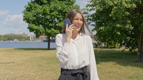 stylish woman in park chatting on phone, blurry city in background