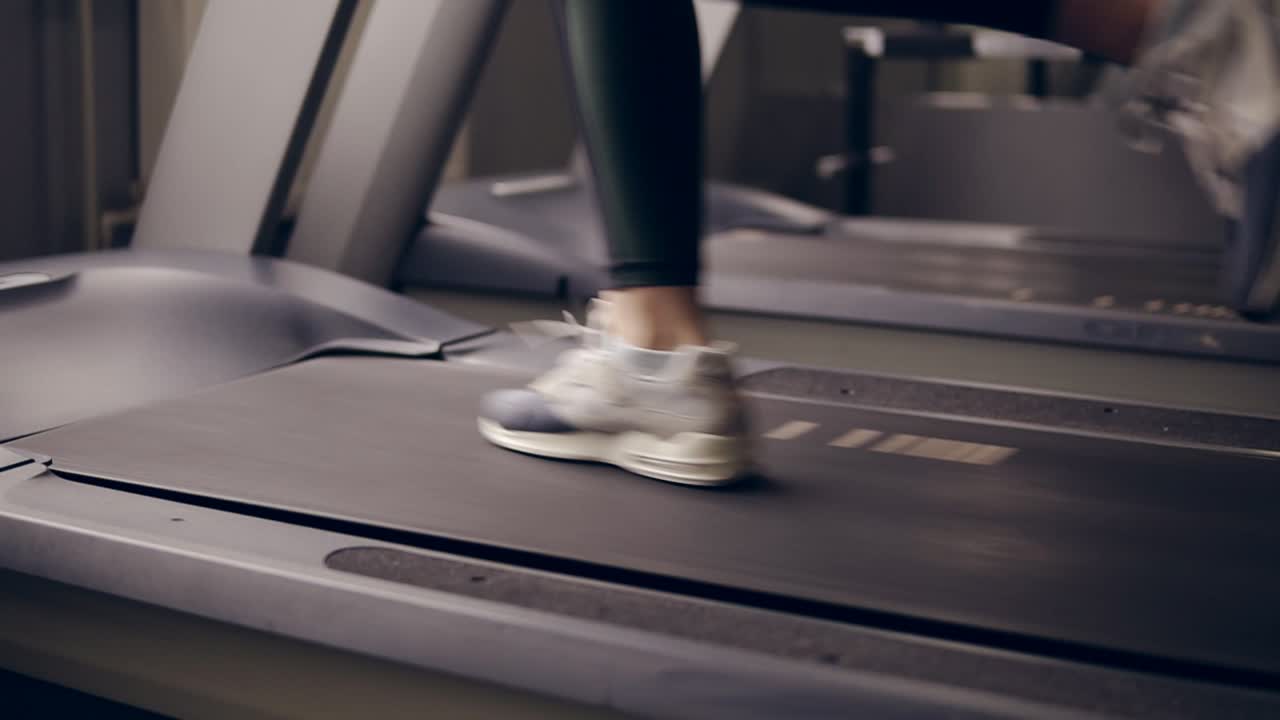 Slow motion footage of female legs in fancy sneakers running on treadmill.