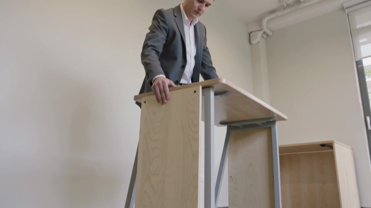 Mand i gråt jakkesæt placerer venstre hånd, sænker sidepanel på træskrivebord på kontoret og tjekker justering.