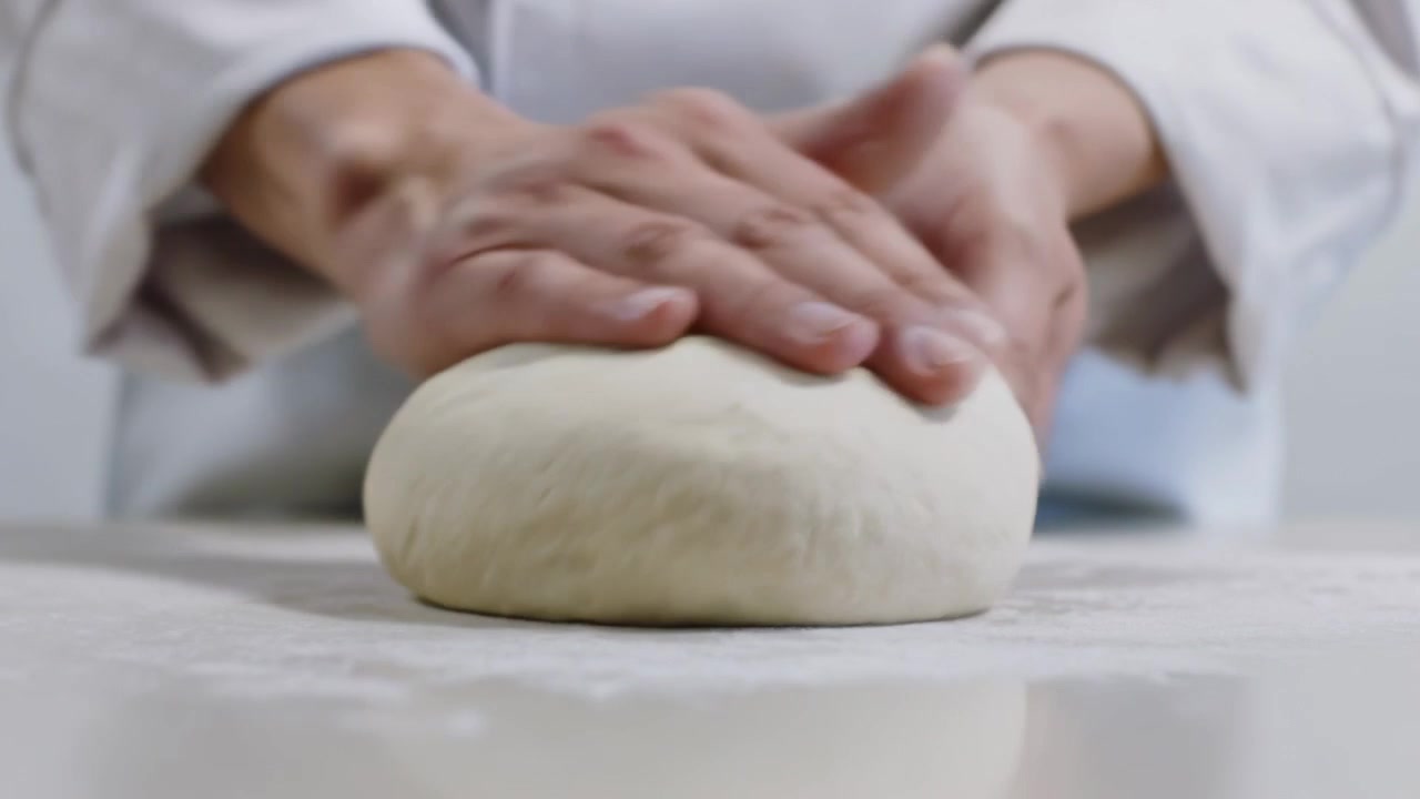 Sollevando l'impasto su un piano di lavoro infarinato, uno chef in camice bianco arrotola e ripiega l'impasto per la lievitazione.