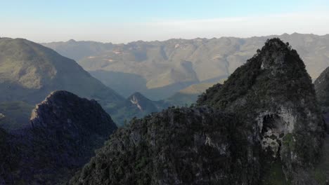 Wide-Aerial-Shot-slowly-descending-facing-a-mountainscape-with-a-cave-at-Dong-Van,-Vietnam,-Happiness-Road,-Ha-Giang-Loop