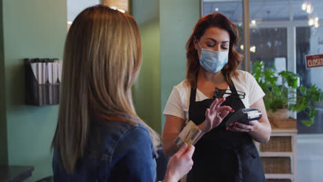 peluquera que usa una máscara facial recibiendo el pago de una cliente femenina