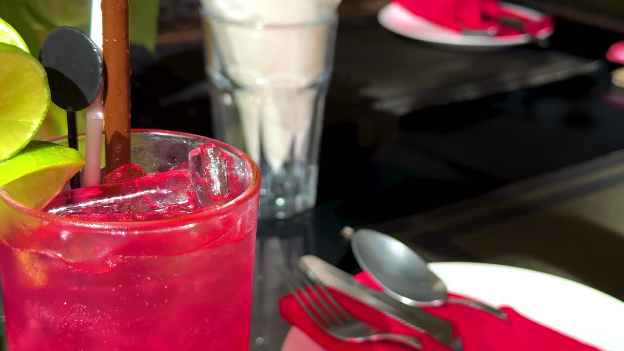 A close-up of a red drink with lime and straw on a table setting.