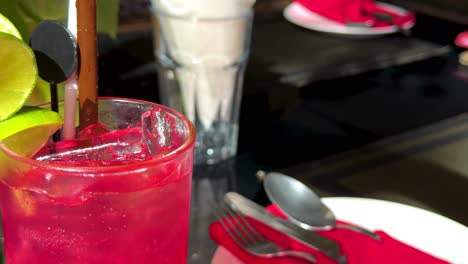 a close-up of a red drink with lime and straw on a table setting.
