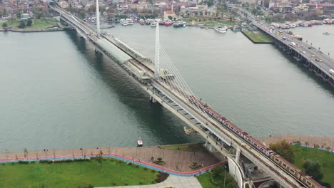 aerial drone circling the halic metro bridge as a train crosses the bosphorus river during a cloudy morning in istanbul turkey