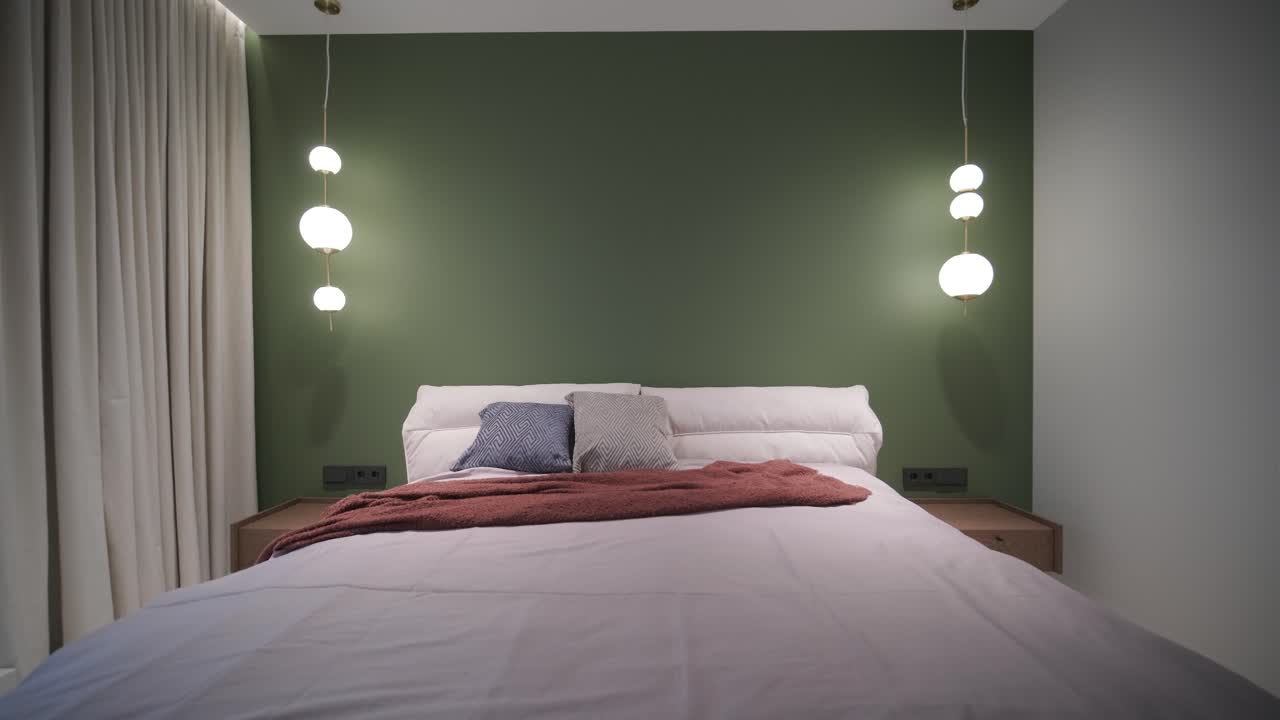 una escena de dormitorio serena con una cama de peluche adornada con un lanzamiento de color óxido, acentuada por una pared de característica verde oscuro y una vista a un baño luminoso, evocando una sensación de comodidad moderna