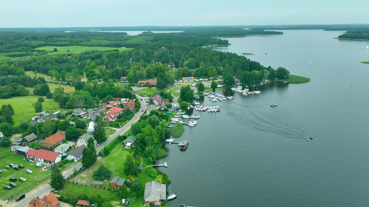 Lakeside view with houses, trees, and boats along the shore under an overcast sky