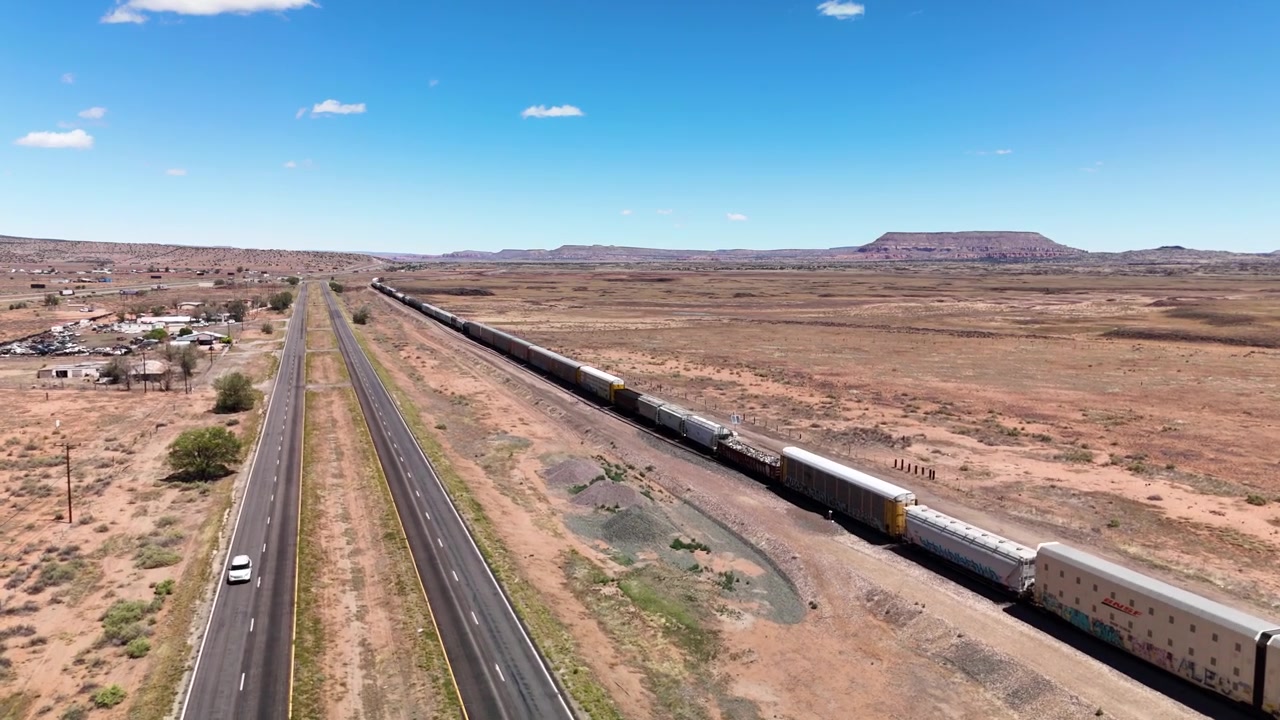 Aerial view of a long freight train traveling through the sunny American desert landscape next to a highway