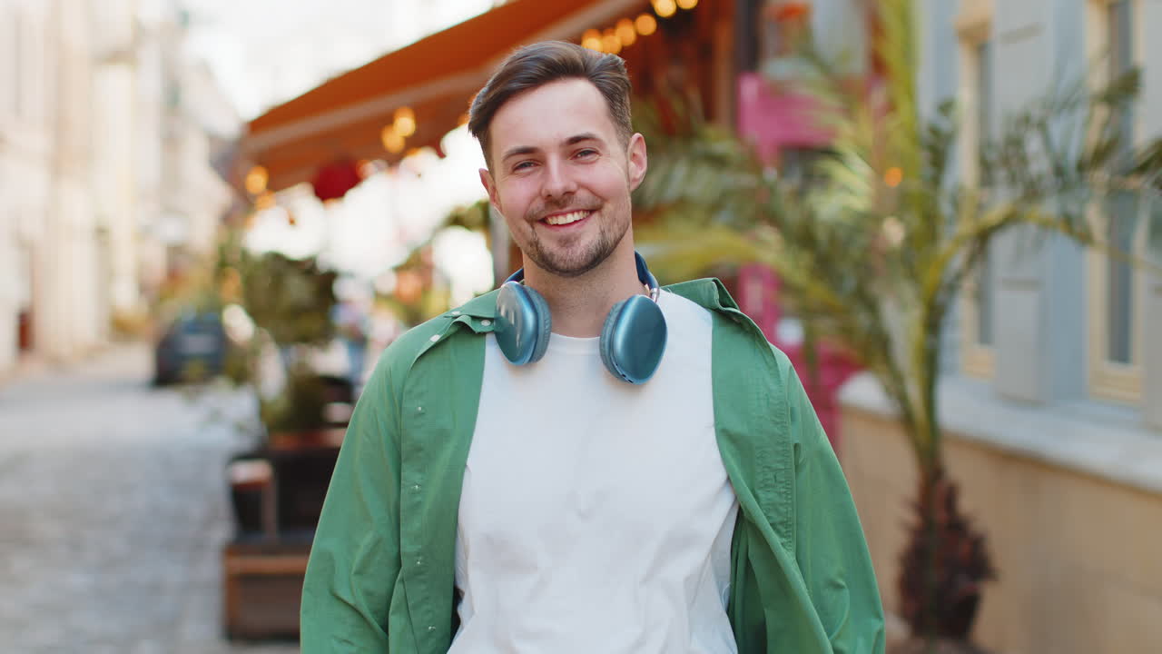 Portrait of smiling young male tourist in casual clothes with wireless headphones around neck