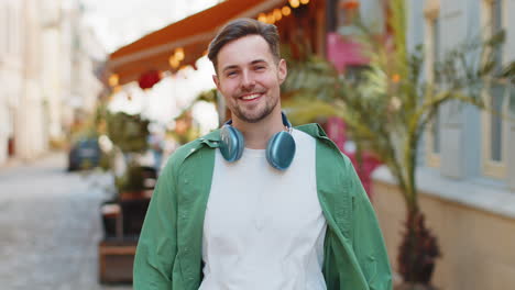 portrait of smiling young male tourist in casual clothes with wireless headphones around neck