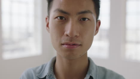 close up portrait of young asian teenager man looking serious focused at camera in apartment windows background