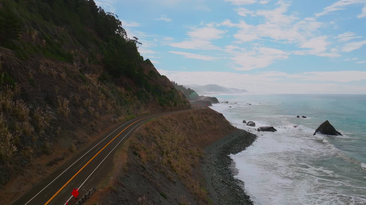 Shoreline Pacific Coastal Highway 1 DeHaven Westport Fort Bragg aerial drone California rugged Coastline blue sky surf waves crashing boulder rocks mountain side clouds Pacific Ocean forward motion