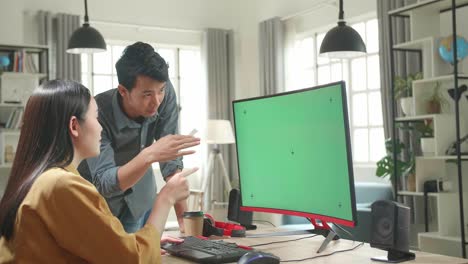 Asian Female Works With Her Male Colleague On A Project On Her Personal Computer With Mock-Up Green Screen. They Work In A Creative Loft Office
