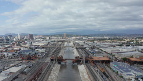 AERIAL:-View-over-Los-Angeles-River-Bridge-Being-Built-under-Construction-Site-with-Overcast-Cloudy-Sky