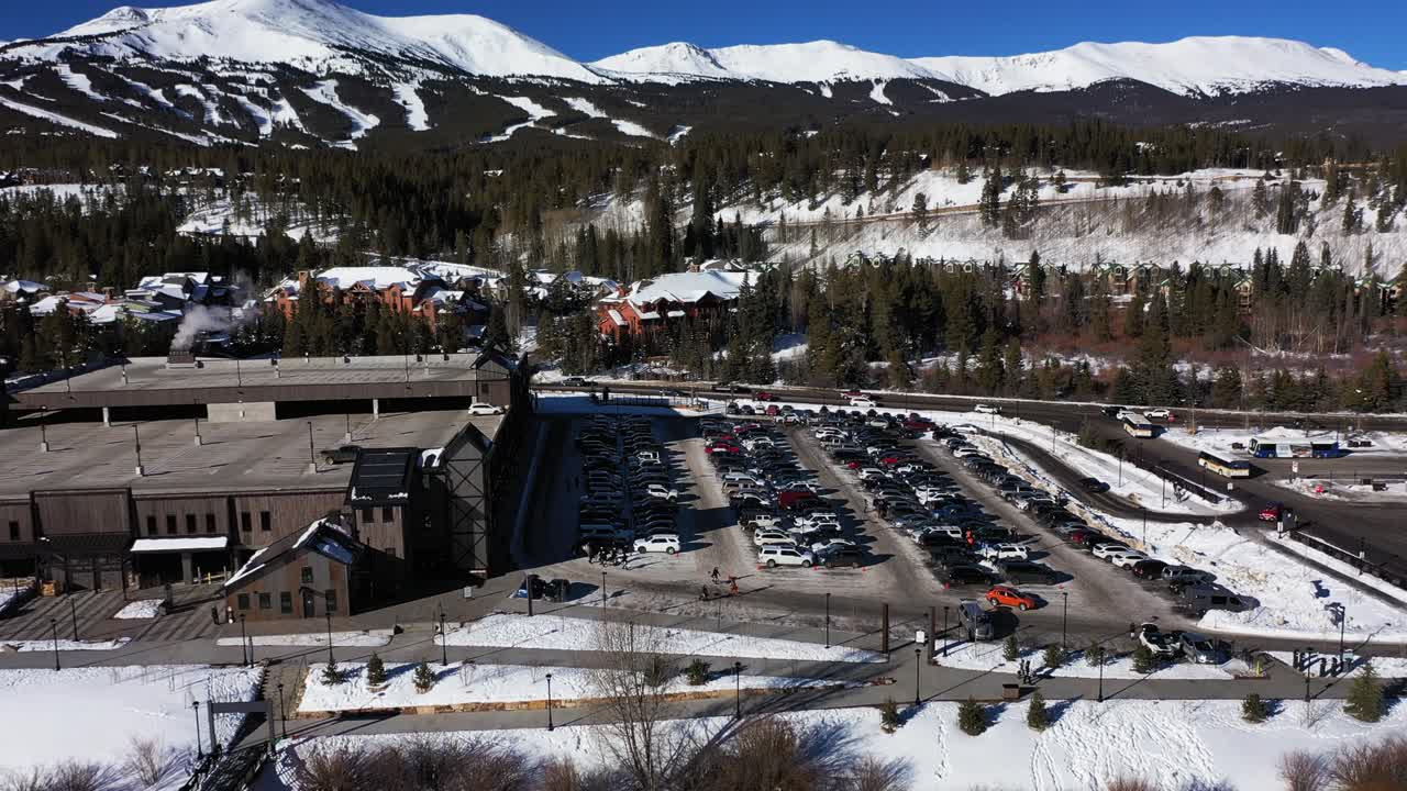 산이 있는 눈 덮인 주차장에 서 있는 다양한 브랜드와 색상의 많은 자동차의 드론 뷰