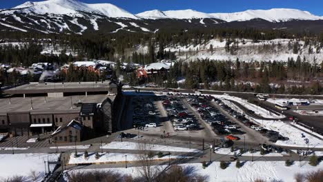 drone view of a large number of cars of different brands and colors standing in a snowy parking lot with mountains