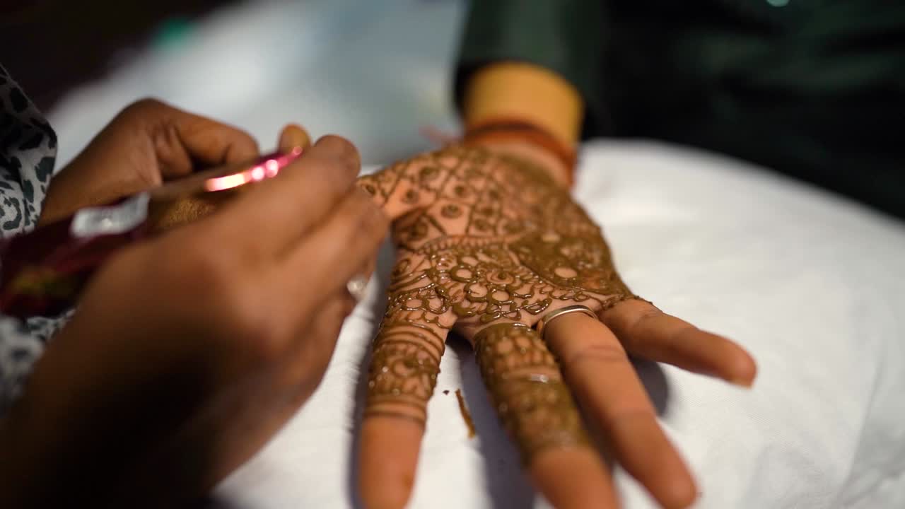 Un artista di mehndi che realizza intricati design con l'henné sulla mano dello sposo durante una tradizionale cerimonia nuziale indiana