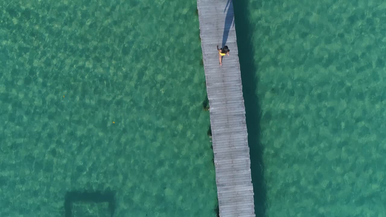 부두에서 혼자 걷는 노란색 비키니 입은 소녀의 공중, 카메라 다운