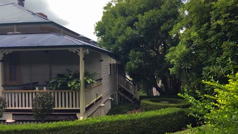 Smooth-slow-cinematic-reveal-shot-of-a-classic-traditional-country-Queenslander-house,-nestling-in-neatly-manicured-landscaped-garden