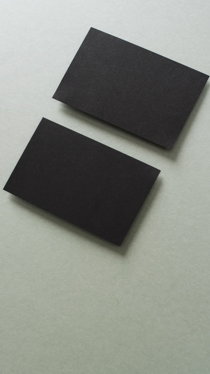 Vertical video of two black business cards arranged on grey background, copy space, slow motion