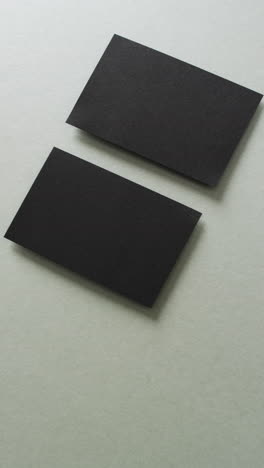 vertical video of two black business cards arranged on grey background, copy space, slow motion
