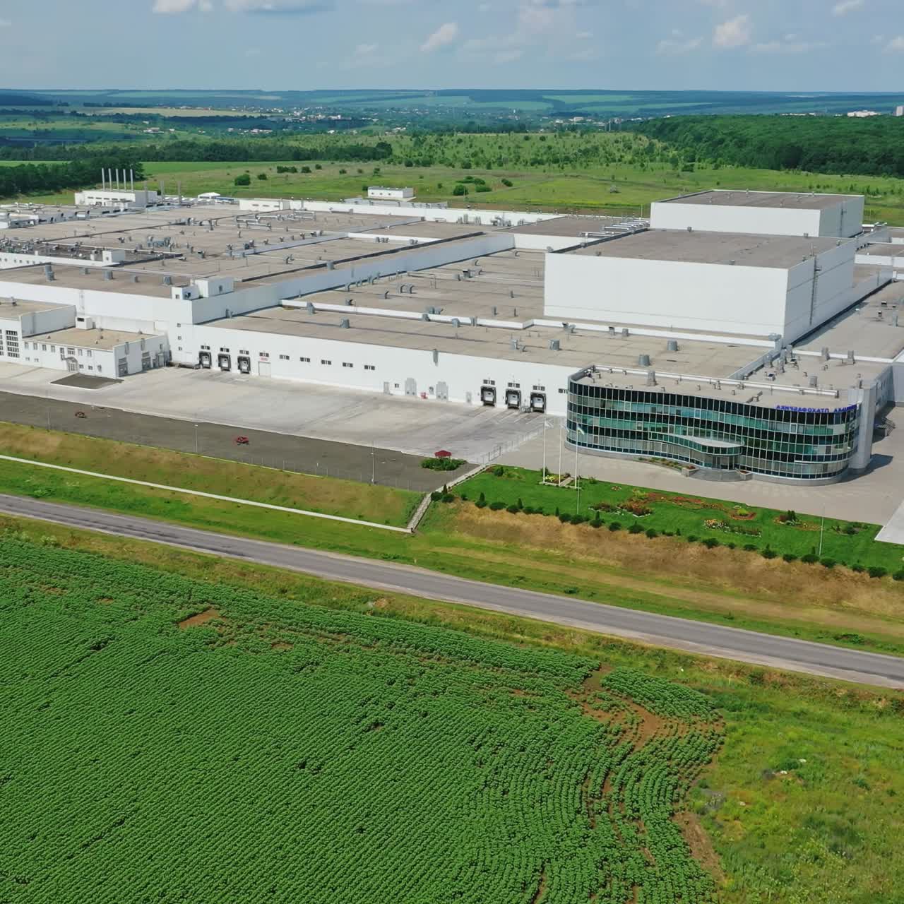 Innovative factory in the countryside. Panoramic view on industrial plant on green landscape. Camera rising up. Aerial view.