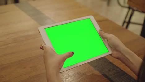 mujer con la mano sosteniendo una tableta con una pantalla verde en blanco y los dedos tocando y deslizando en la pantalla.
