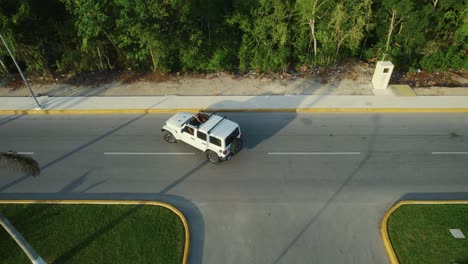 Drone-shot-view-of-white-car-driving-turn-around-on-road-in-Tulum,-Mexico