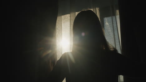 a woman will open the curtain towards a sunny day. back view