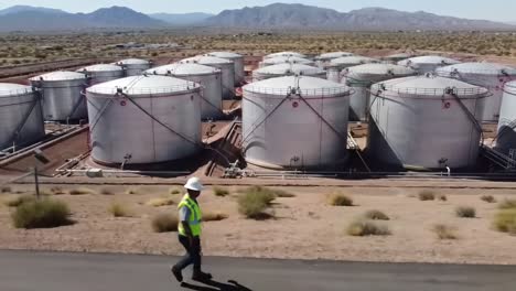 a foreman inspects oil storage tanks in a desert landscape, overseeing operations in a remote energy facility with a scenic mountain backdrop