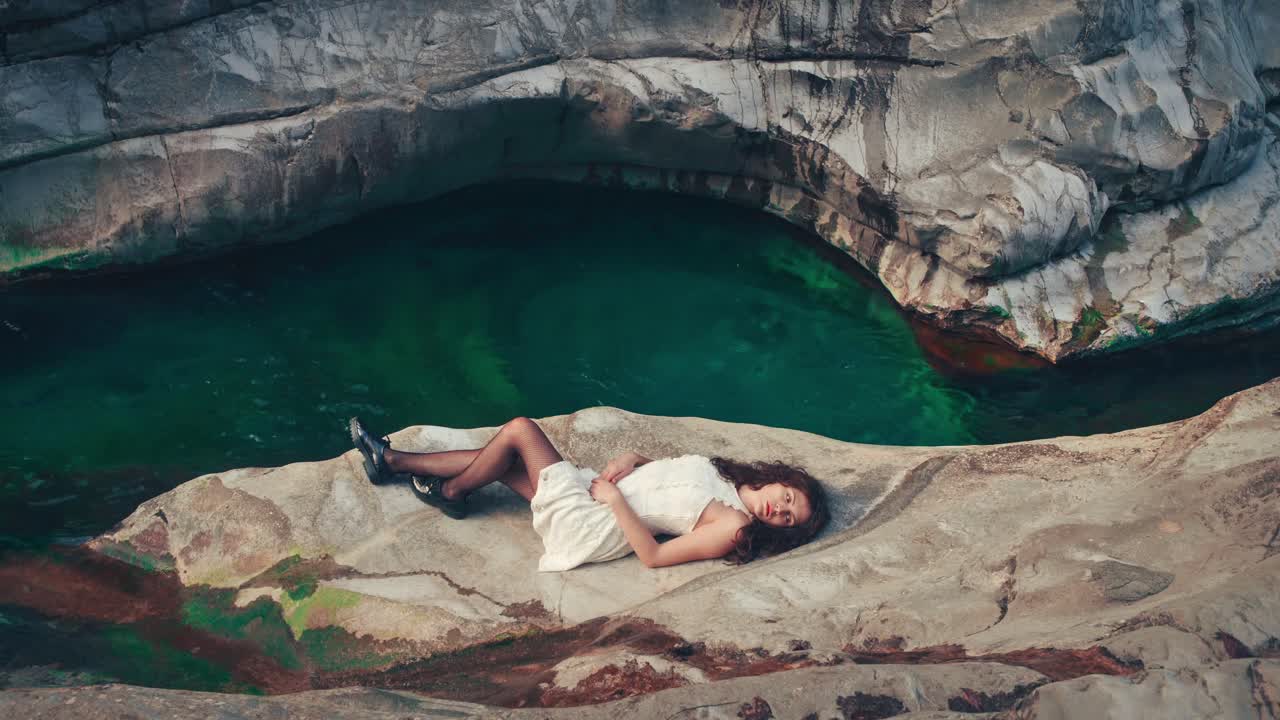 cinemagraph de 4k: bucle de video sin costuras de una joven modelo morena con un vestido blanco al borde de un desfiladero junto a un río de montaña azul