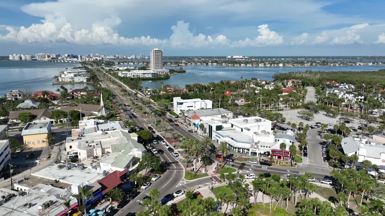 Aerial rising shot of famous st Armand’s circle roundabout in Sarasota, Florida. Sunny day with blue sky and cars on street. Sarasota downtown in distance. Wide shot.