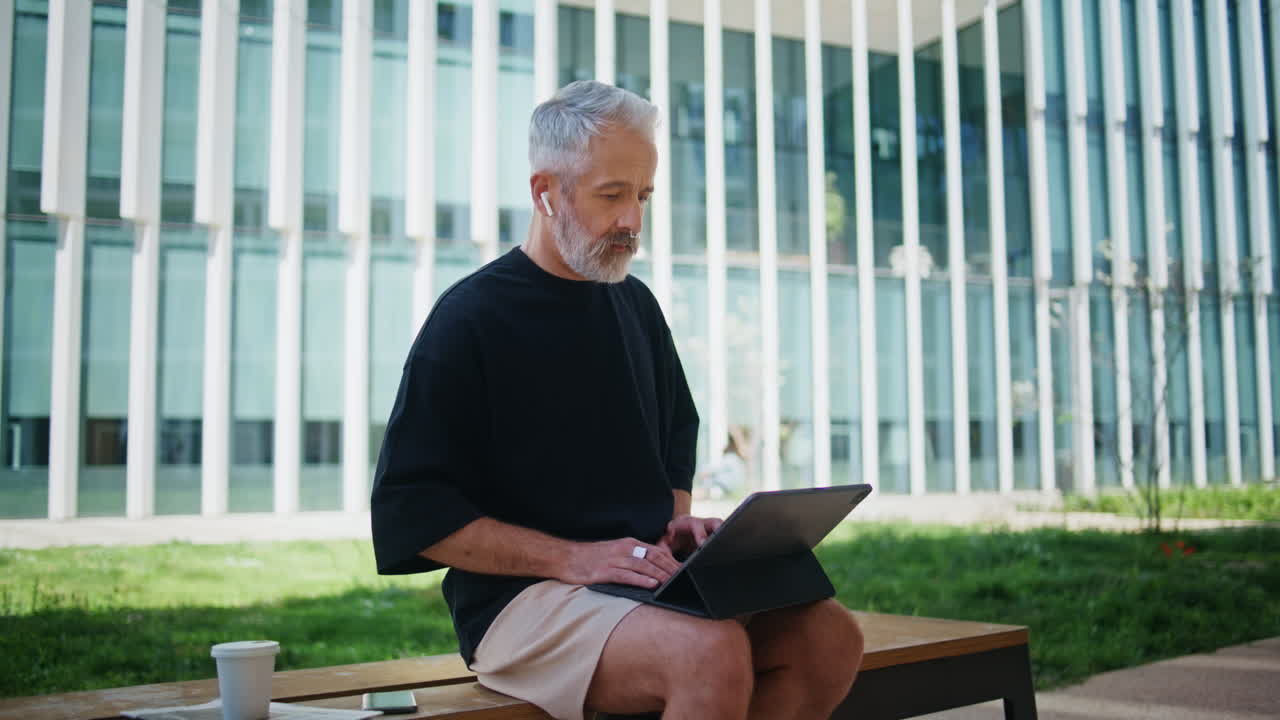 Older manager working remotely in city park. Focused senior typing computer