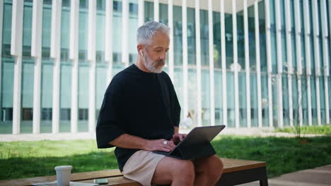 older manager working remotely in city park. focused senior typing computer
