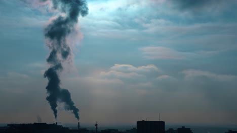 4k-Sonnenuntergang-Windige-Wolken,-Die-Blaue-Himmel-Mit-Silhouettengebäuden-Und-Doppelten-Schornsteinen-Verwandeln,-Die-Den-Himmel-Mit-Dunklen,-Nebligen-Rauchschwaden-Und-Der-Sonne-Füllen,-Die-Die-Hintergrundreflexion-Beschattet