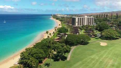 Aerial-view-of-white-birds-over-a-golf-course-and-a-long-sandy-beach-in-Maui,-Hawaii