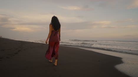 young woman in red dress walking alone in a tropical sandy seacoast